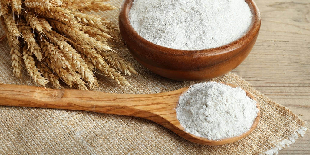 wood bowl filled with all purpose flour and a wood spoon with flour on a wooden table to show foods that start with a