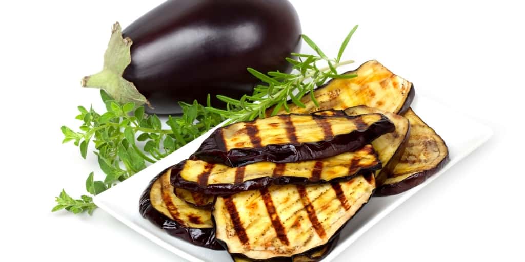 Aubergines also known as eggplant sliced thinly and grilled sitting on a white plate