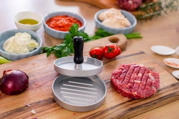 best burger press on a cutting board with one patty made and various vegetables
