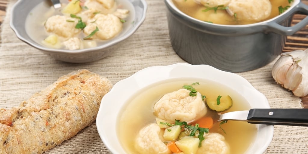 chicken and dumplings in a white bowl with a spoon and a baguette on the side