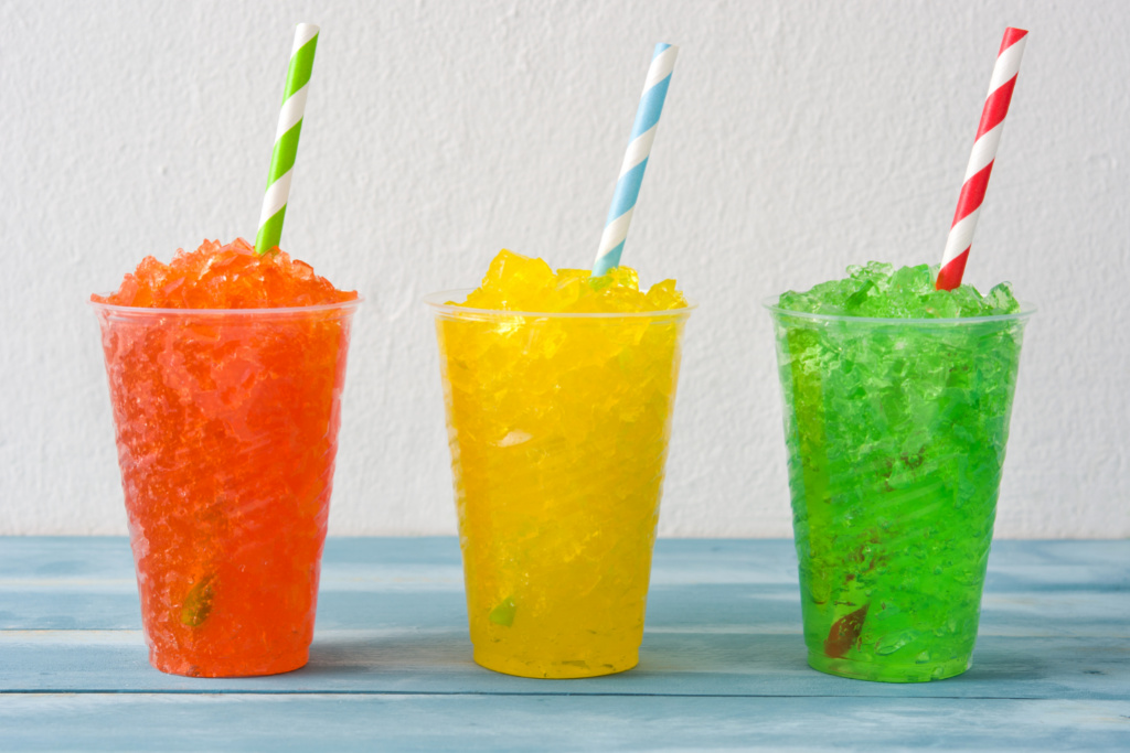 three colorful ice slushie drinks with striped straws in them